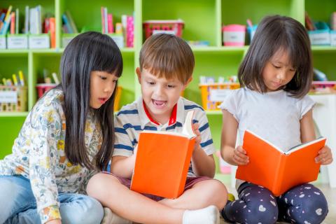 Three young children read together.